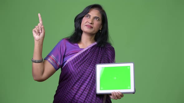 Mature Beautiful Indian Woman Thinking While Showing Digital Tablet and Pointing Finger Up