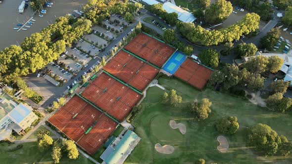 Aerial shot flying above a sport club with clay tennis courts and a professional golf green field at