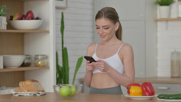 Young Woman Using Smartphone in Kitchen