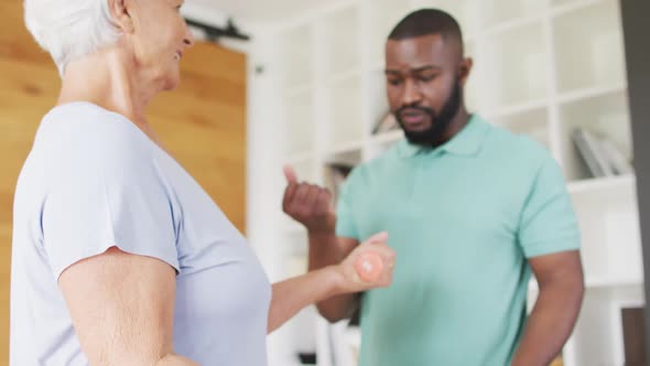 Video of african american male physiotherapist exercising with caucasian senior woman