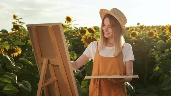 A Woman is Applying Paint to a Canvas That Standing on an Easel