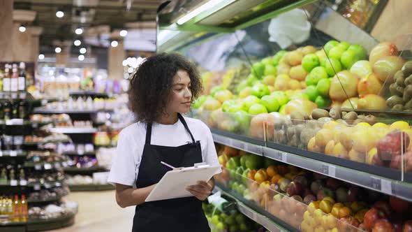 Portrait of African American Female Staff Person Standing in Front of the Fruit Shelves with Tablet