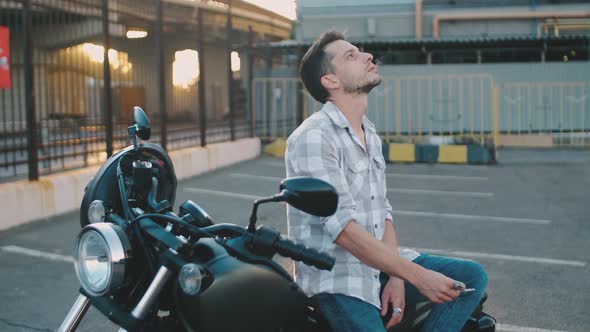 Portrait of Man Motorcyclist Smokes a Cigarette While Sitting on a Motorcycle at Street