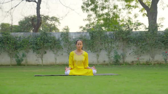 Indian woman doing Padmasana or Lotus yoga pose and chanting Om in a park