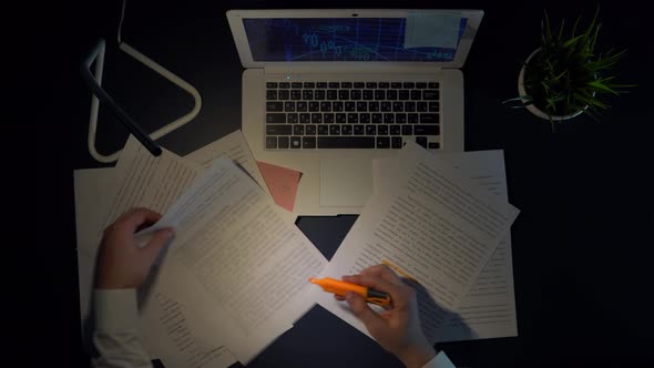 A Man Marks the Words in Documents While Sitting at a Table with a Laptop