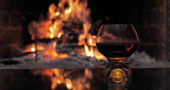 Glass with Cognac on the Background of Fire in the Fireplace