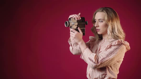 Beautiful Woman In Red Background Looking Through Viewfinder Of A Vintage Camcorder. Retro Concept.