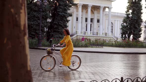 Beautiful Woman Riding a City Bicycle with a Basket and Flowers in the City Center Enjoying Her Time