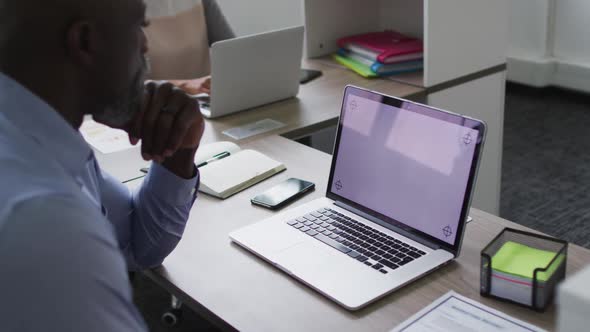 African american businessman sitting at desk and using laptop with copy space on screen in office