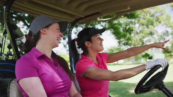 Two caucasian women playing golf riding a golf cart talking and laughing