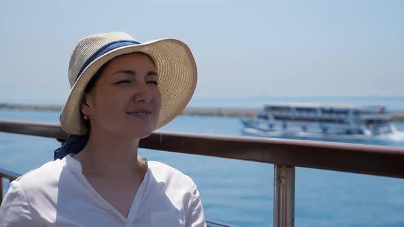 Pretty Woman in Elegant Straw Hat Sits on Ship Deck