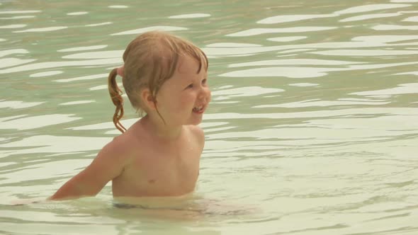 Cute Little Girl is Playing and Waving Her Hands in Small Pool in the Aquapark