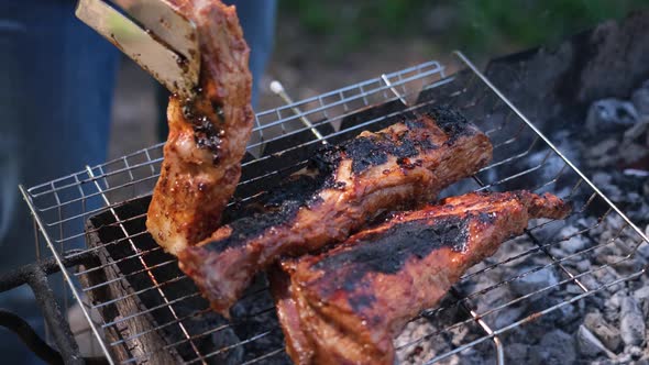 Flipping Delicious Beef or Pork Ribs Frying on a Charcoal Grill with Tongs