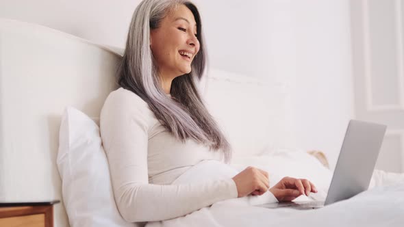 Smiling Asian woman talking by video call on laptop