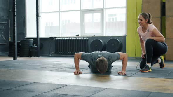 Young Man Doing Push-ups Exercising in Gym with Female Coach Enjoying Exercise