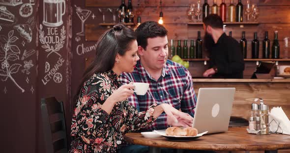 Caucasian Couple Looking at Laptop and Drinking Coffee with Croissants