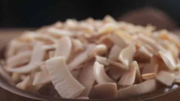 Coconut chips are falling down to wooden bowl close-up