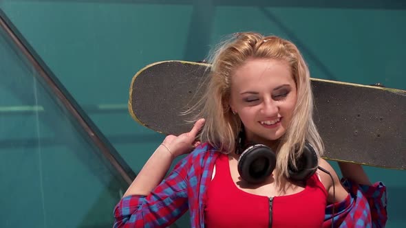 Portrait of Pretty Young Teenage Girl in Headphones Posing with Skateboard