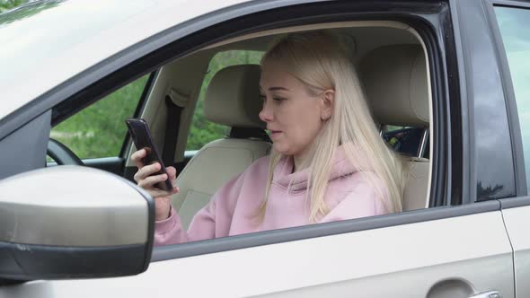 Young woman sitting in a car and using smartphone.