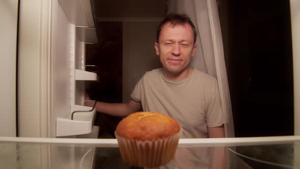 A man opens the refrigerator at night on the shelf is one cupcake, a disgruntled man