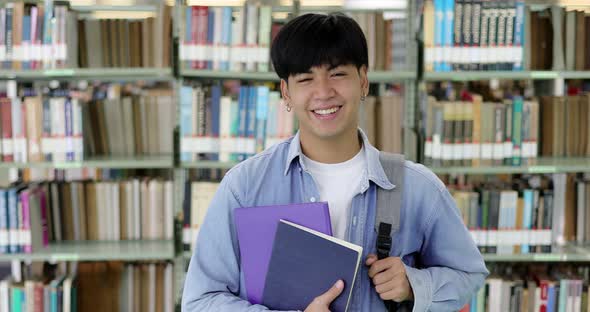 Zoom in shot happy Asian handsome student with books smiling looking at camera in library.