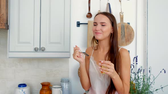 Happy Girl Sitting On Kitchen Table And Eating Yogurt For Breakfast