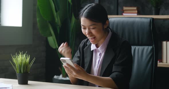 Asian Woman Sit at Desk Office Hold Smartphone Receive Message From Bank Feels Incredible Happy