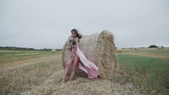 Stunning Lady in Blowing Evening Dress with Bouquet Stands in Poses at Haystack