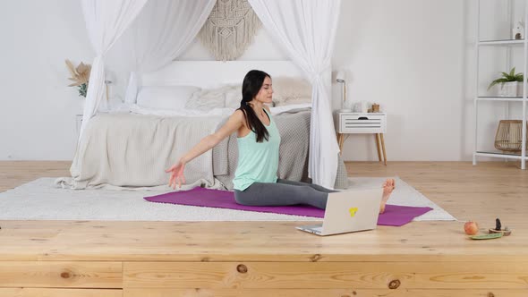 Peacful Happy Young Woman Practicing Yoga on Mat with Laptop