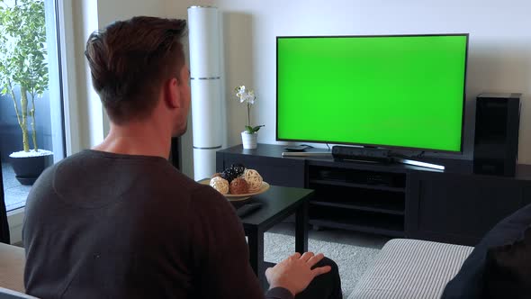 A Man Cheers and Gesticulates Excitedly at a TV with a Green Screen