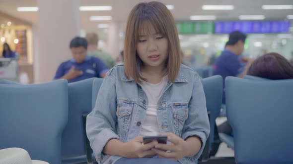 Asian woman checking her smartphone while sitting on chair in international airport