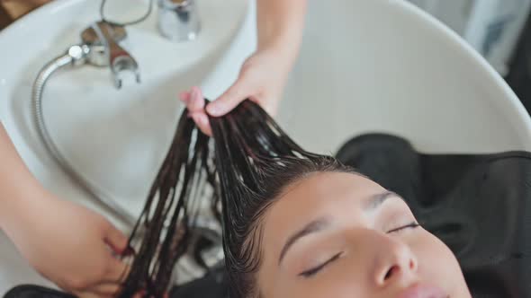Caucasian young woman lying down and close eye on salon washing bed getting hair washed in salon.