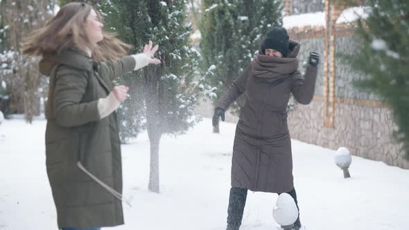 Snowball Fight of Two Joyful Young Caucasian Women Outdoors