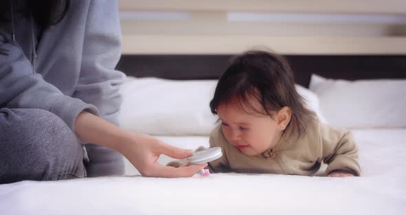 Baby Lies on Her Stomach on the Bed in the Nursery and Licks the Nipple Holder