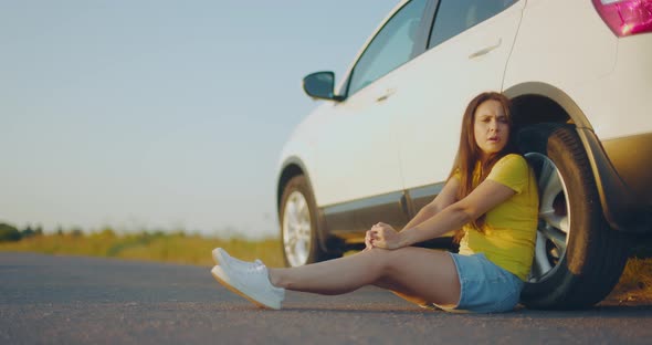 Young Upset Girl Sitting Next to Broken Car on Side of Road