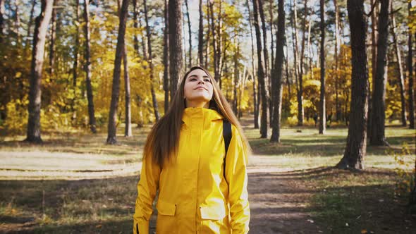 Young Woman in Parka Coat is Smiling Taking Deep Breath and Looking Around While Walking in Autumn