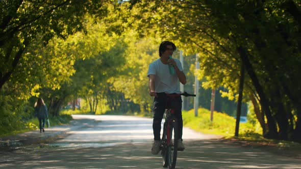 Young Sportive Man in White Shirt Riding a Bike and Drink Water From the Bottle