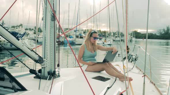 Yacht's Board with a Woman Browsing a Laptop While Sitting on It