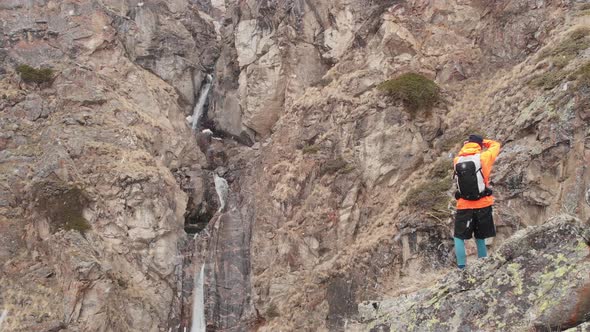 Aerial View of a Young Male Photographer with a Camera in His Hands Stands on a High Rock in a Gorge