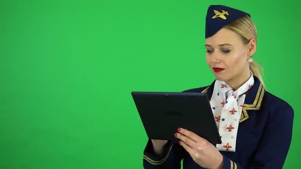 A Young Beautiful Stewardess Works on a Tablet with a Smile - Green Screen Studio