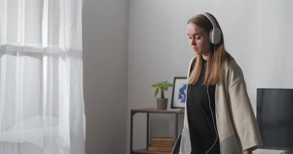 Young Woman Is Using Hoover for Cleaning Home Listening To Song By Earphones and Dancing Cheerfully