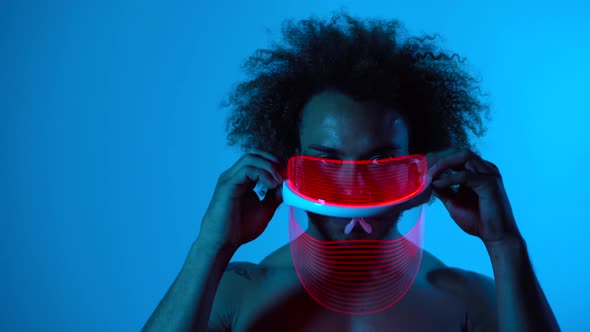 Man wearing light therapy mask against blue wall