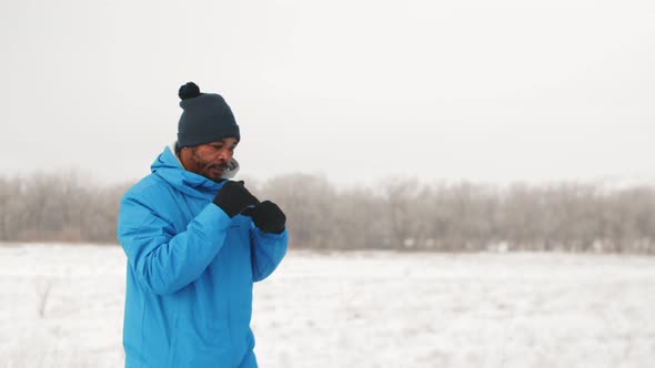 AfricanAmerican Man in Warm Sports Clothes Trains to Boxing Outdoors in Winter Front View