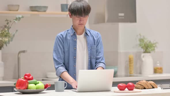 Asian Man Working on Laptop in Kitchen