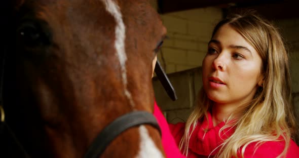 Woman wearing rein to horse in stable 4k