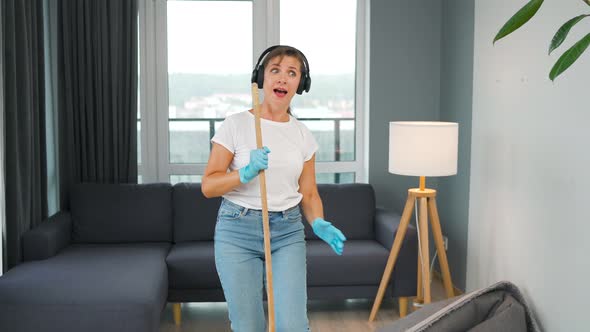 Woman in Headphones Cleans the House and Have Fun Singing with a Broom Like a Star at a Concert