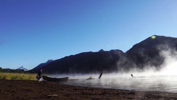 fishermans prepare on a steam fog lake with mist and volcano in background