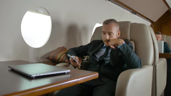 Businessman in Formal Suit Traveling on His Private Jet and Chatting on Cell Phone