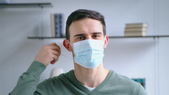 Young man taking off medical mask and smiling while looking at camera