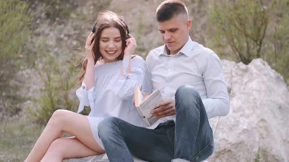 Man and Woman Sitting on Stone and Reading Book Together